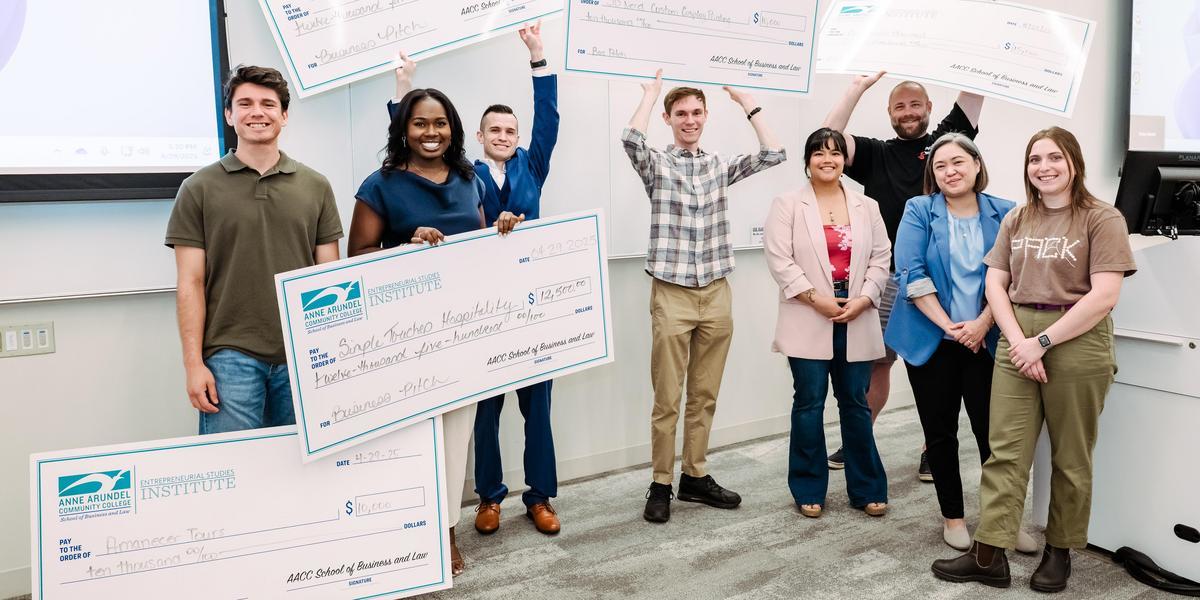 A group of students, some holding large checks, pose for a photo.