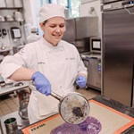 Nicole pouring purple liquid onto a silicone mat in a commercial kitchen.