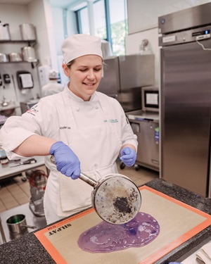 Nicole pouring purple liquid onto a silicone mat in a commercial kitchen.