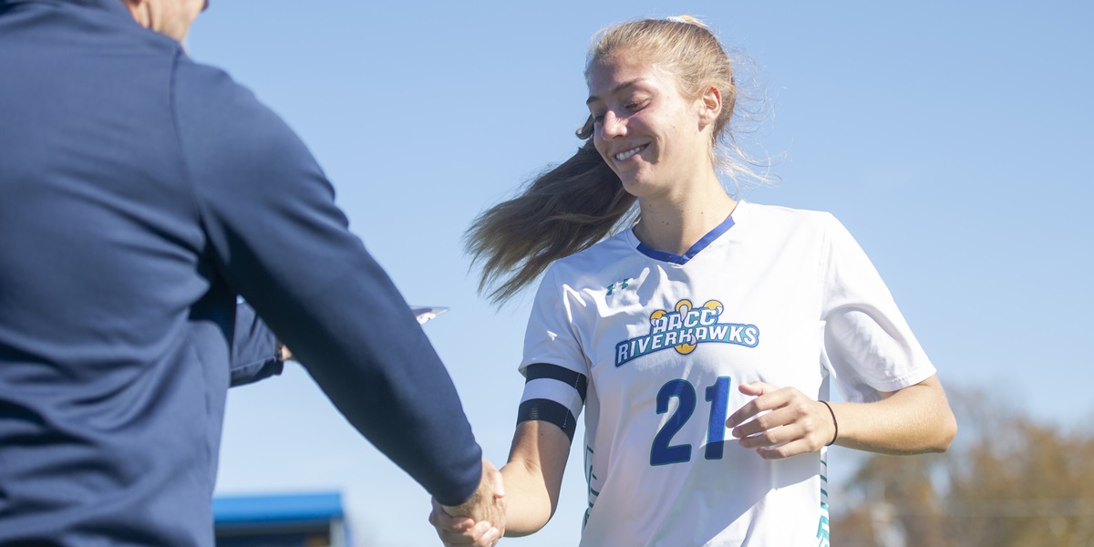Tina Tinelli shaking hands with a person off screen before receiving an award after the soccer championship game.