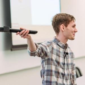 A student holds a device while speaking at the Business Pitch competition.