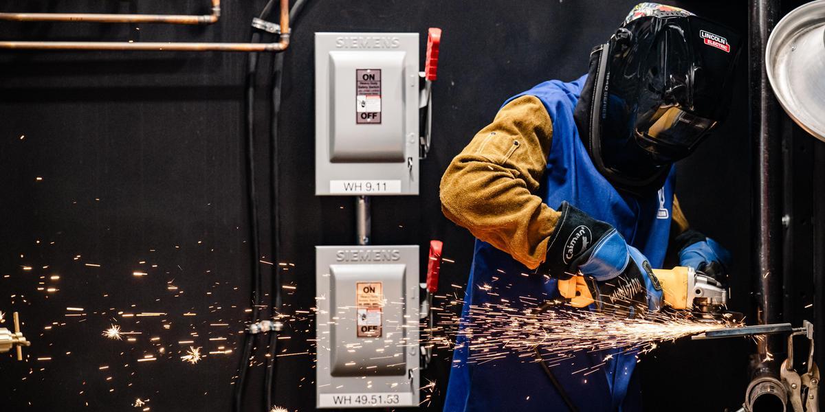 Person wearing protective gear and working with welding tool, producing sparks.