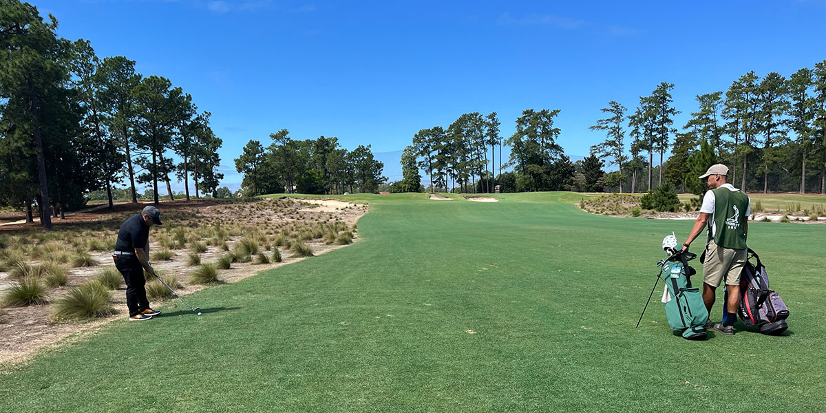 Sean Moorhouse playing golf as a caddie looks on.