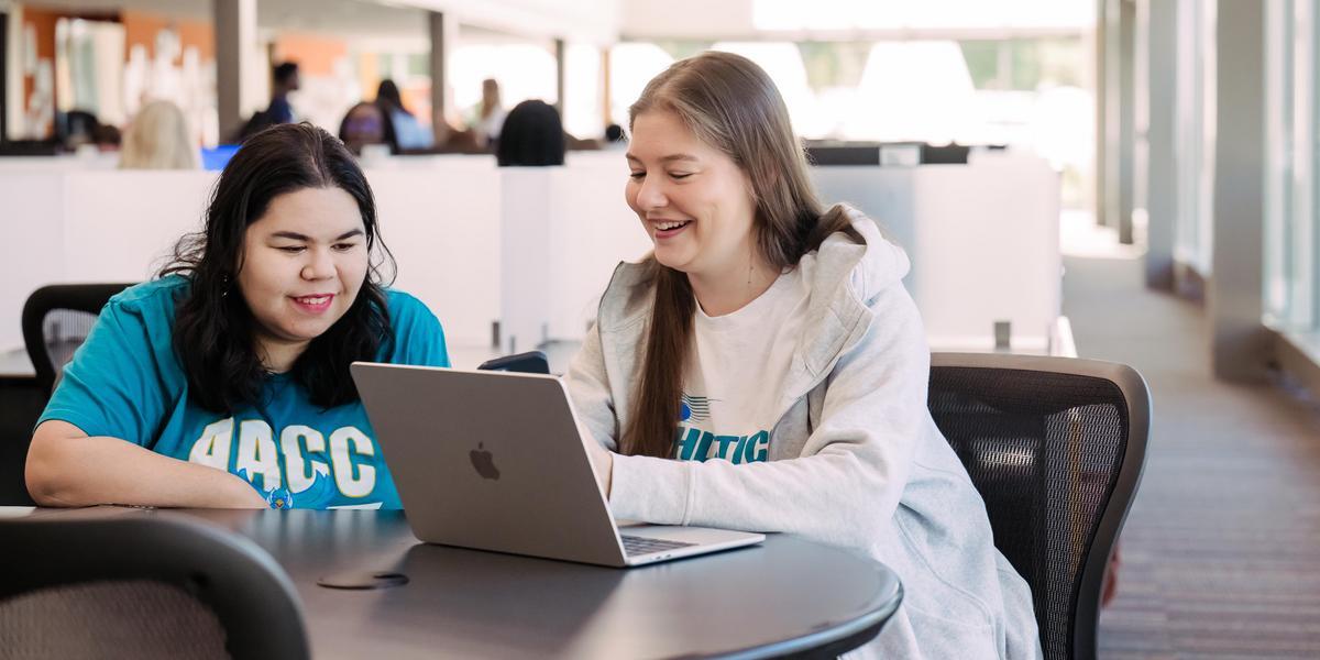 Two students sitting at a table looking at a laptop.