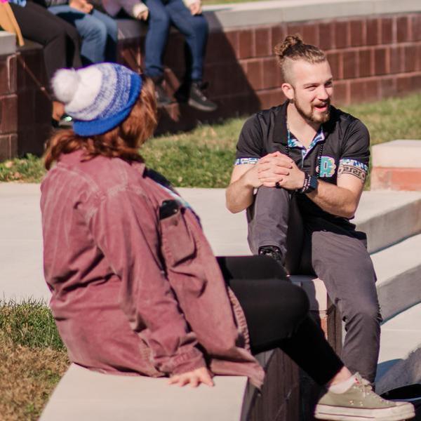 Group of students talking to one another outside in amphitheater.