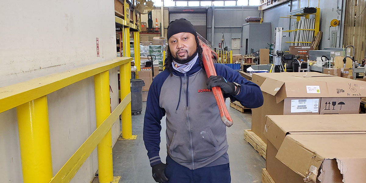 Teddy Strong standing in a warehouse with a piece of equipment over his shoulder.