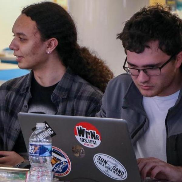 Students eating, talking and using a laptop in the Hawk's Nest dining area