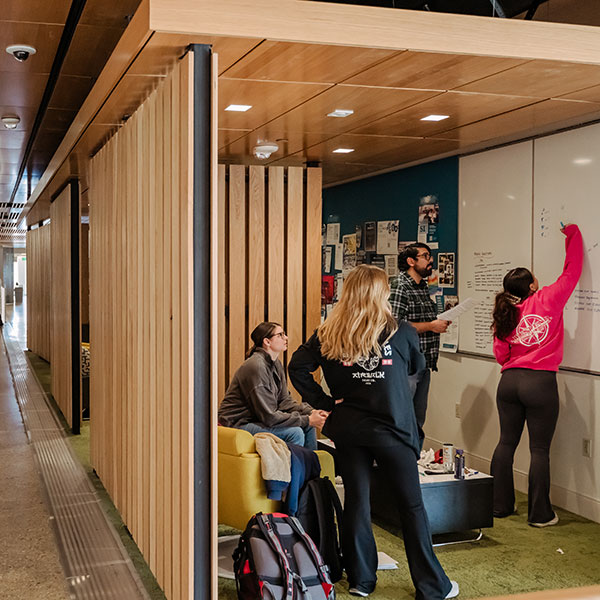 Student writing on white board while other students look on in collaborative studying area.